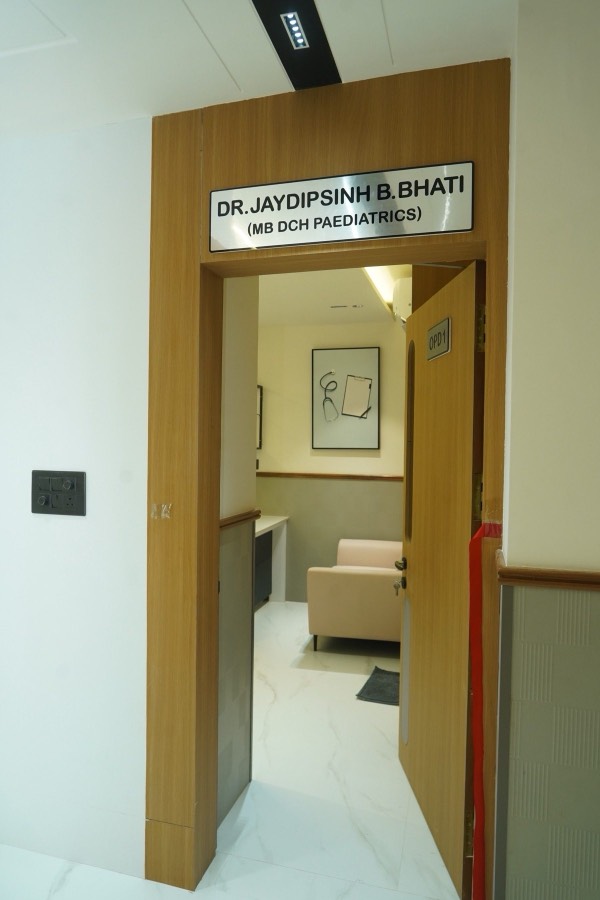 The paediatrics OPD doorway in warm teak, with the doctor’s nameplate mounted beside it.
